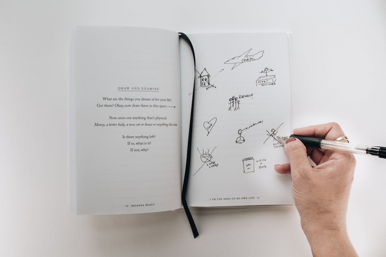 Hand writing and doodling in a journal, encouraging creativity.